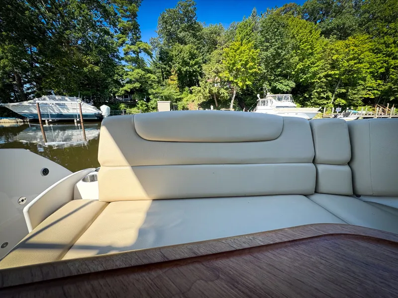 Slide: The Image of 2016 Rinker 290 Express boat interior with beige seating, docked near lush greenery. - 36