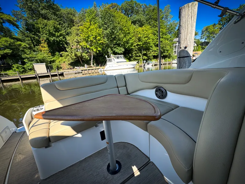 Slide: The Image of 2016 Rinker 290 Express boat interior with cushioned seating and wooden table, docked by lush greenery. - 37