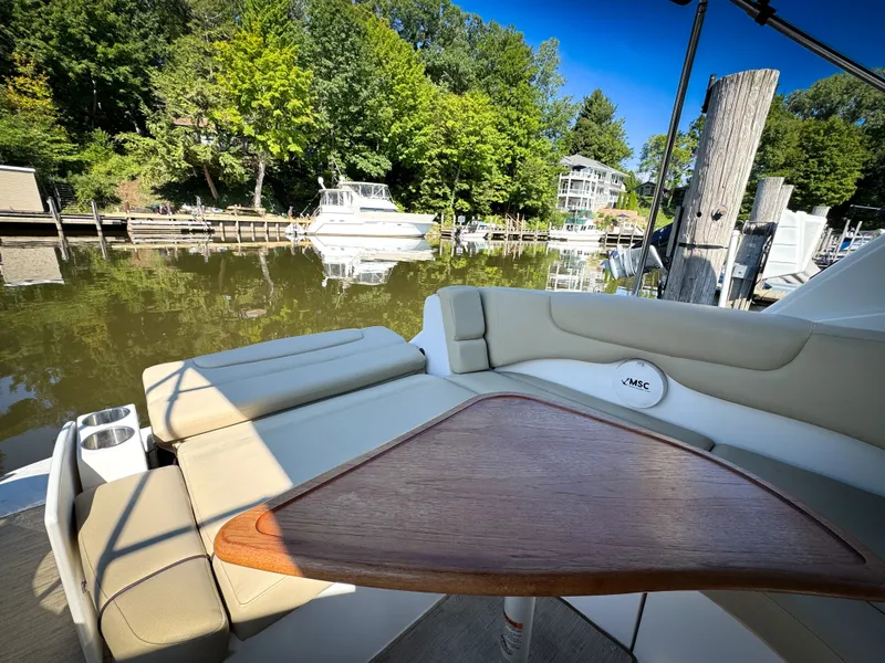 Slide: The Image of 2016 Rinker 290 Express boat interior with seating and table, docked by a serene waterfront. - 39