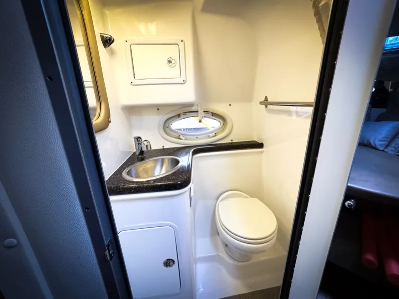 Slide: The Image of 2016 Rinker 290 Express boat bathroom with sink, toilet, and porthole window. - 48