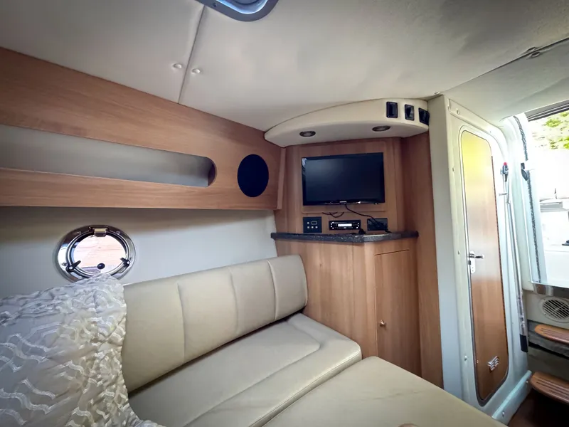 Slide: The Image of 2016 Rinker 290 Express cabin interior with TV, beige seating, and wood accents. - 5