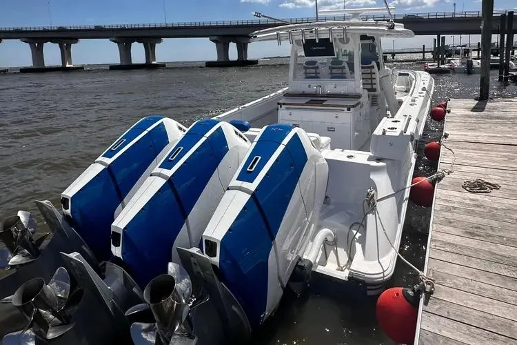 Slide: The Image of 2025 HCB 42 Lujo boat docked, featuring triple outboard engines, under a clear sky. - 16