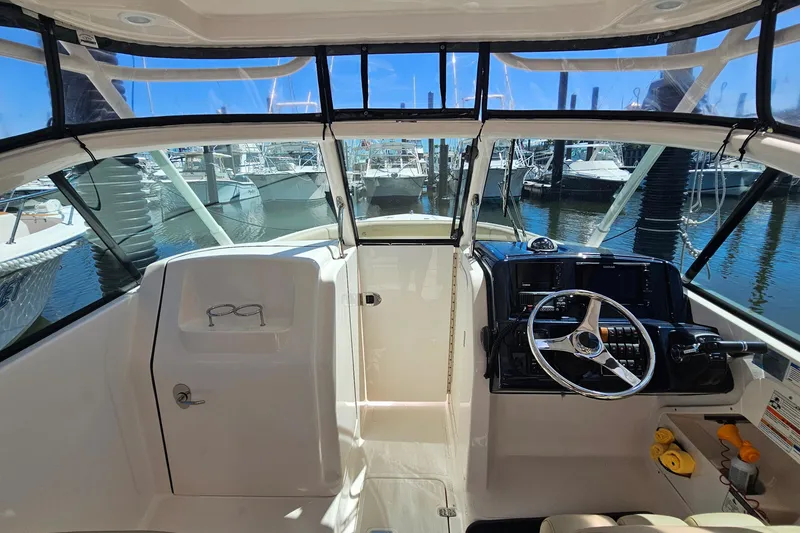 Slide: The Image of 2016 Pursuit DC 265 Dual Console boat interior with steering wheel and marina view. - 17