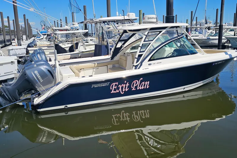 Slide: The Image of 2016 Pursuit DC 265 Dual Console boat named "Exit Plan" docked in marina. - 2