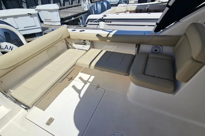 Slide: The Image of 2016 Pursuit DC 265 Dual Console boat interior with beige seating and storage compartments. - 8