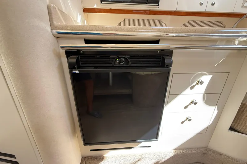 Slide: The Image of 2001 Sea Ray 310 Sundancer interior with compact black refrigerator and storage drawers. - 33