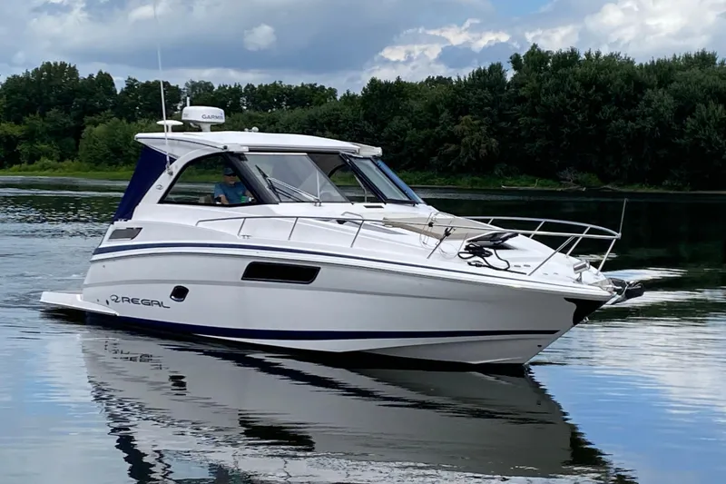 The Image of 2014 Regal 35 Sport Coupe boat cruising on a calm lake with lush green trees. - 0