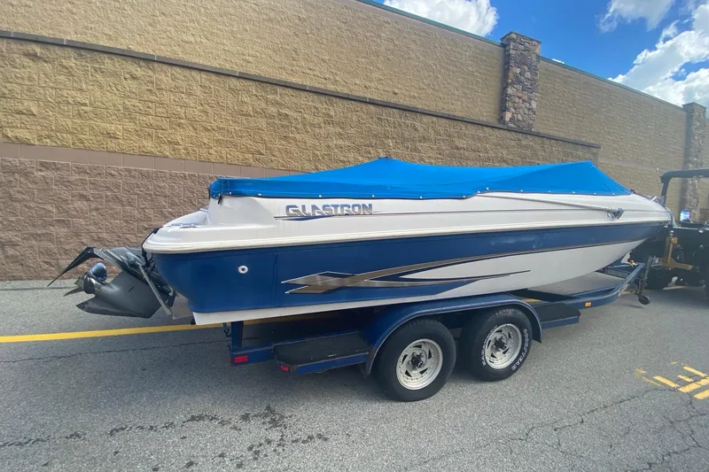 Slide: The Image of 1998 Glastron/Carlson GS225 boat with blue cover on trailer, parked outdoors. - 3