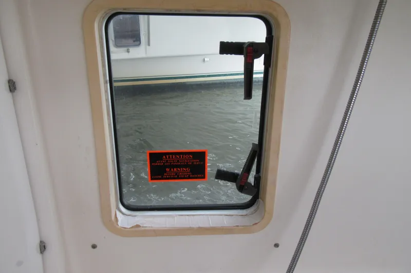 Slide: The Image of Window view from 2001 Catana 471 sailboat, showing water and safety warning label. - 122