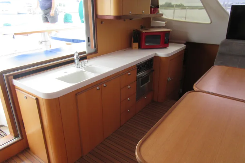 Slide: The Image of 2001 Catana 471 yacht interior kitchen with wooden cabinets, sink, and red microwave. - 97
