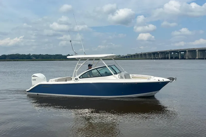 Slide: The Image of 2023 Pursuit DC 246 Dual Console boat on calm water near a bridge under a cloudy sky. - 6