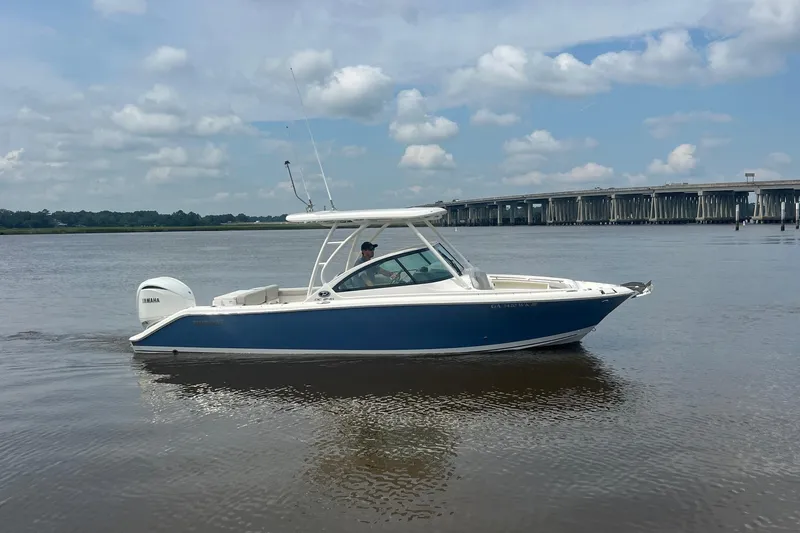 Slide: The Image of 2023 Pursuit DC 246 Dual Console boat on calm water near a bridge under a cloudy sky. - 7