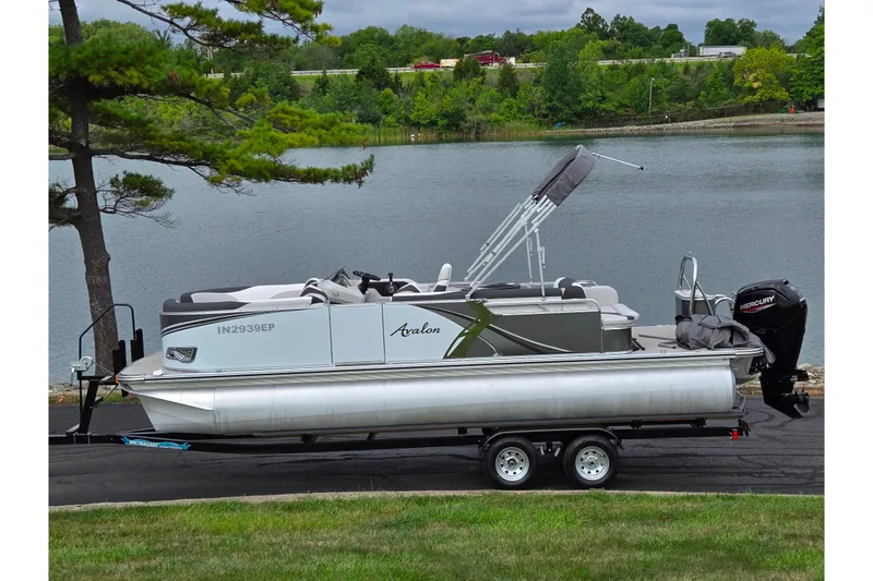 The Image of 2024 Avalon LSZ Cruise Bench pontoon boat on trailer by a scenic lake. - 0