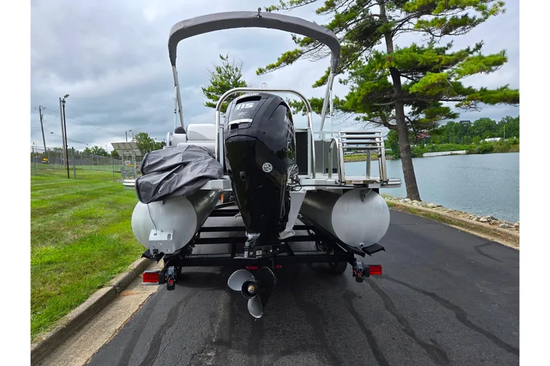 Slide: The Image of 2024 Avalon LSZ Cruise Bench pontoon boat with Mercury outboard motor on a trailer by a lake. - 2