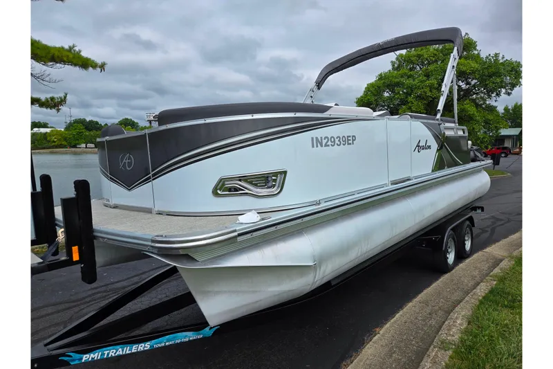 Slide: The Image of 2024 Avalon LSZ Cruise Bench pontoon boat on trailer, parked near a lake. - 8