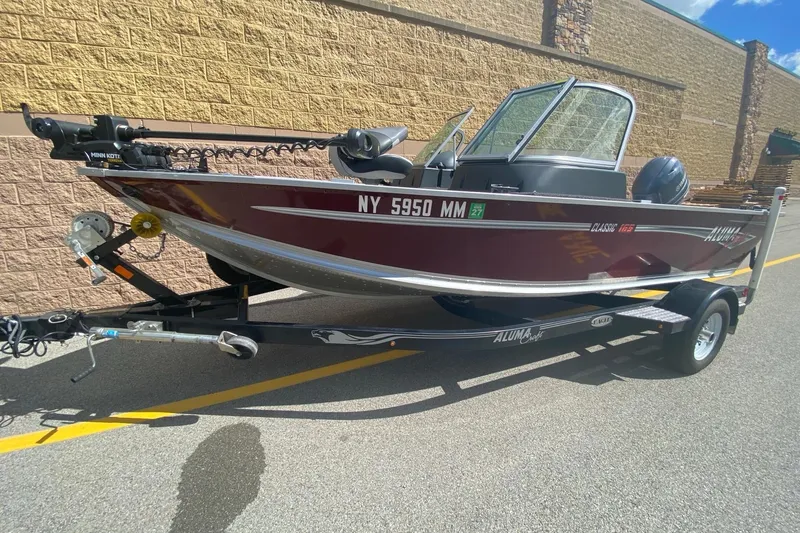 Slide: The Image of 2017 Alumacraft Classic 165 boat on trailer, parked outdoors, with maroon exterior. - 0