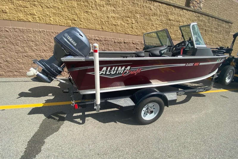 Slide: The Image of 2017 Alumacraft Classic 165 boat with Yamaha motor on trailer, parked outdoors. - 1