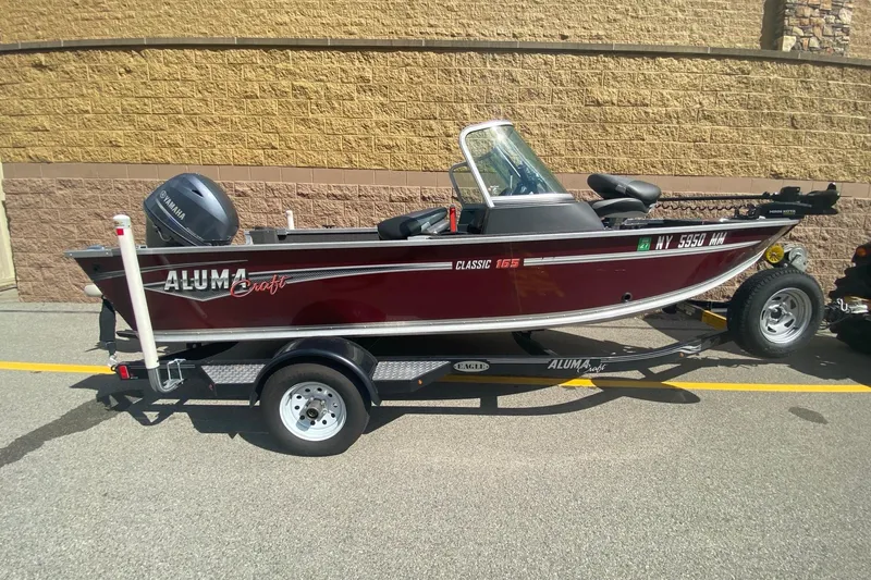 Slide: The Image of 2017 Alumacraft Classic 165 boat on trailer, parked outdoors, featuring Yamaha outboard motor. - 2