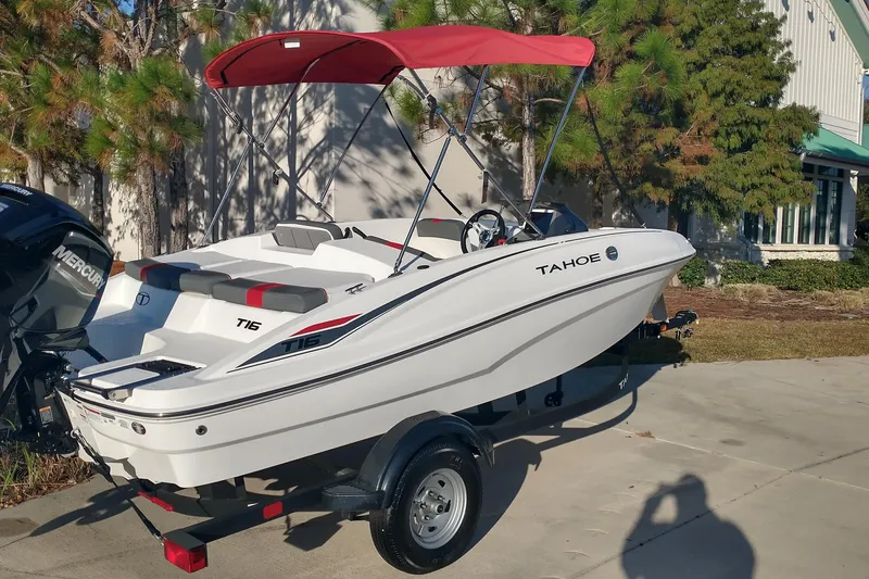 Slide: The Image of 2026 Tahoe T16 boat with red canopy on a trailer, parked outdoors. - 2
