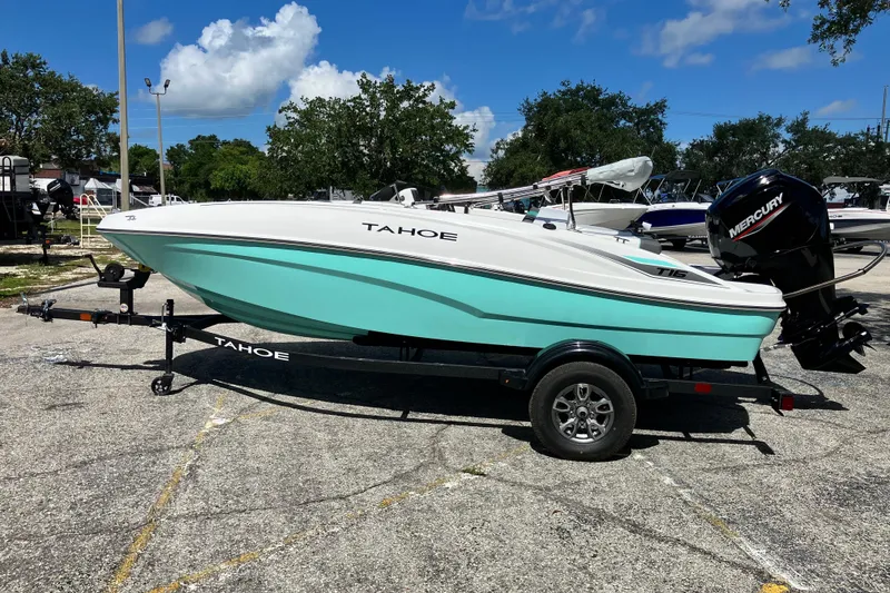 Slide: The Image of 2026 Tahoe T16 boat on trailer, turquoise hull, parked outdoors under blue sky. - 2
