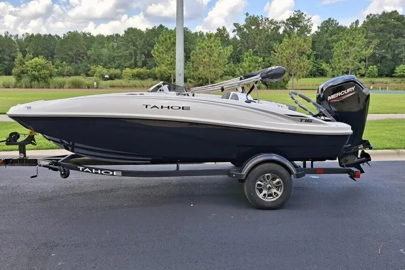 The Image of 2026 Tahoe T16 boat on trailer with Mercury engine, parked on asphalt near greenery. - 0