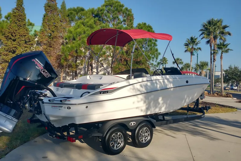 Slide: The Image of 2026 Tahoe T21 boat with red canopy on trailer, parked outdoors. - 2