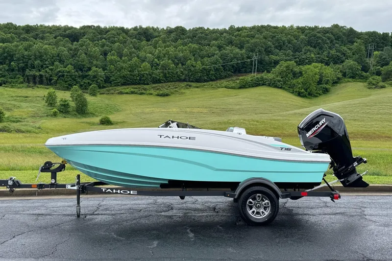 Slide: The Image of 2026 Tahoe T16 boat on trailer, parked on road with lush green landscape background. - 2