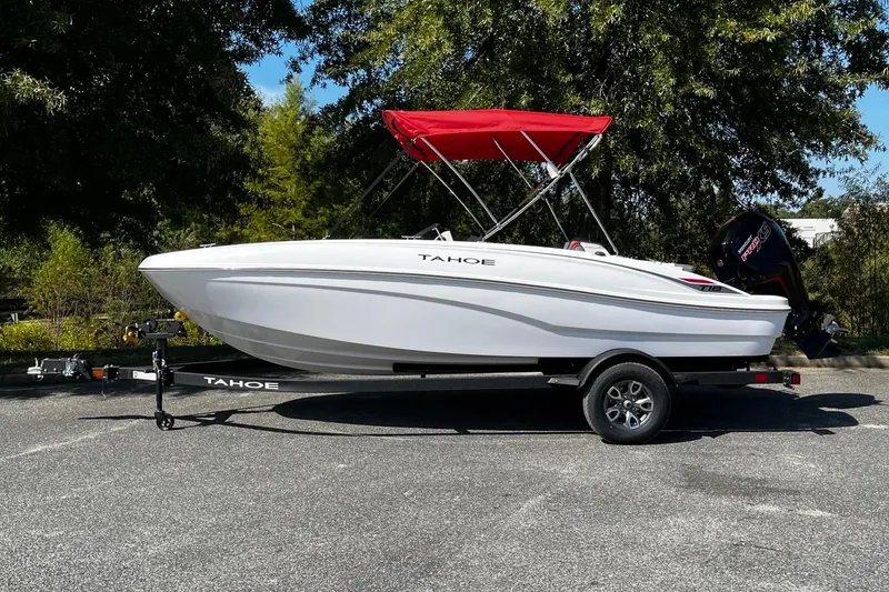 Slide: The Image of 2026 Tahoe T18 boat with red canopy on trailer, parked outdoors. - 2