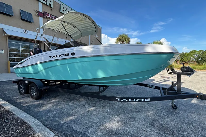 The Image of 2026 Tahoe T21 boat on trailer, turquoise hull, parked outside dealership. - 0