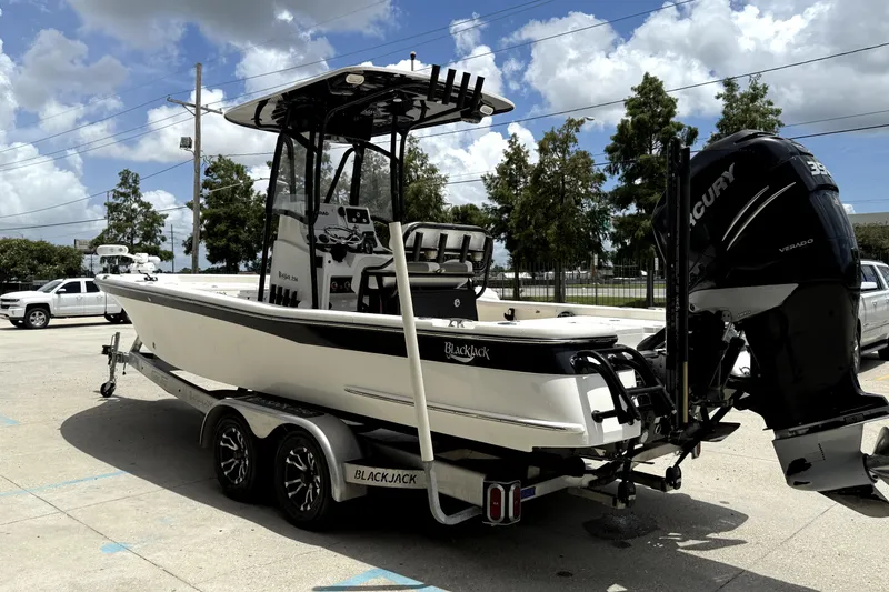 Slide: The Image of 2019 BlackJack 256 boat on trailer with Mercury engine, parked outdoors under cloudy sky. - 5