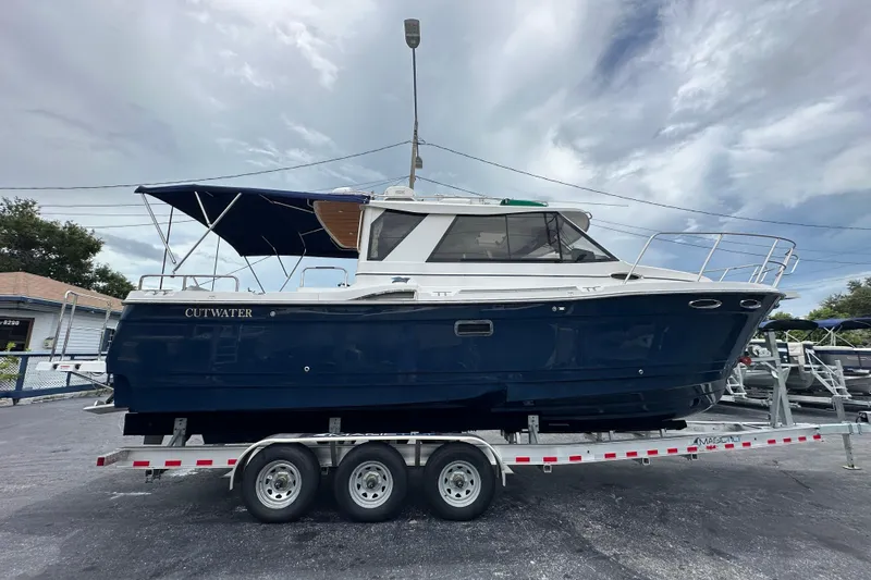 Slide: The Image of 2020 Cutwater C-28 boat on trailer, blue hull, parked outdoors under cloudy sky. - 2