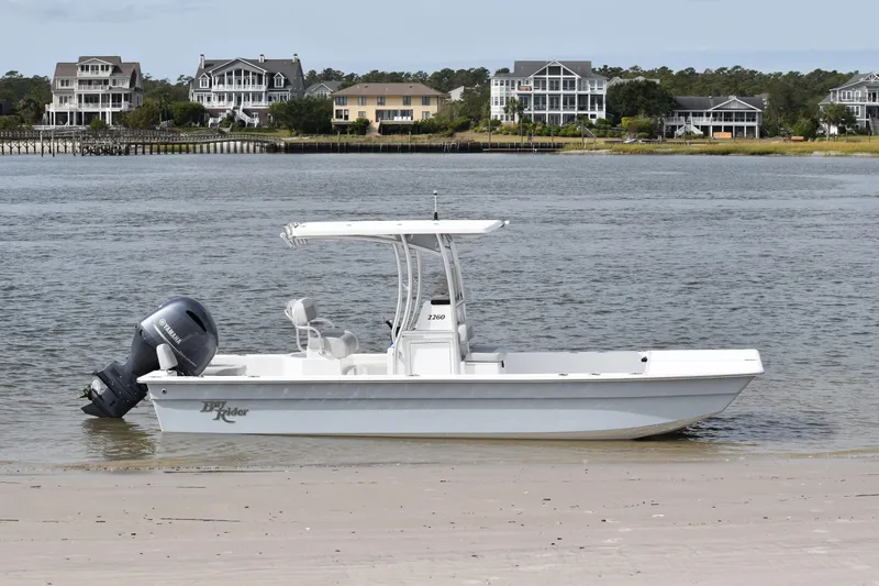 Slide: The Image of 2025 KenCraft 2260 Bay Rider Skiff on a sandy shore with waterfront homes in the background. - 4