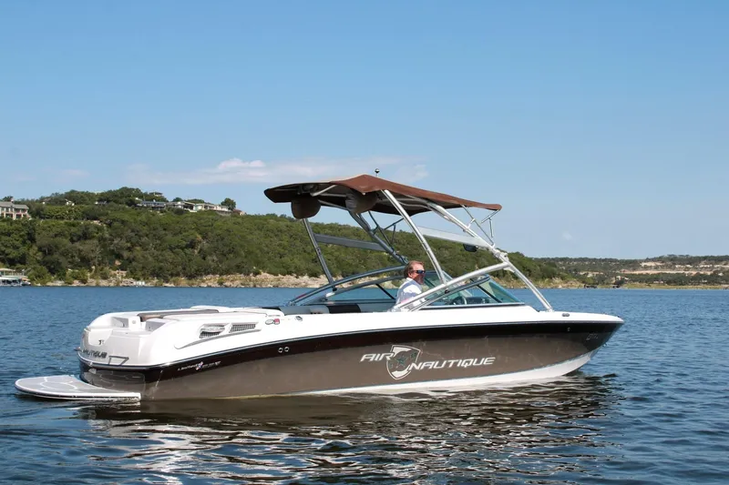 Slide: The Image of 2008 Air Nautique Crossover 236 boat on a scenic lake with lush green hills. - 23