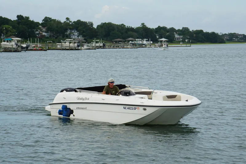 Slide: The Image of 2017 Bayliner Element F21 boat cruising on a calm lake near a marina. - 2