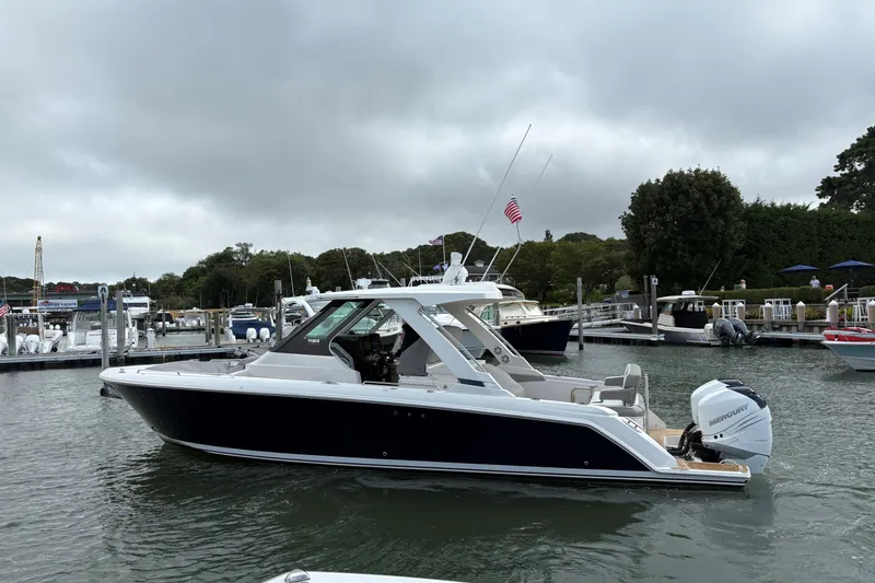 Slide: The Image of 2022 Tiara Yachts 34 LS in marina, sleek design, overcast sky, American flag visible. - 24