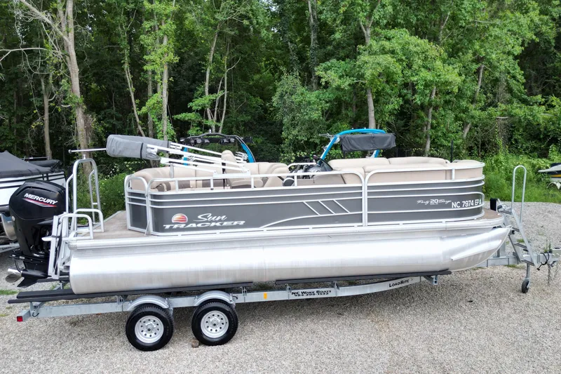 Slide: The Image of 2020 Sun Tracker Party Barge 20 DLX pontoon boat on trailer, surrounded by trees. - 3
