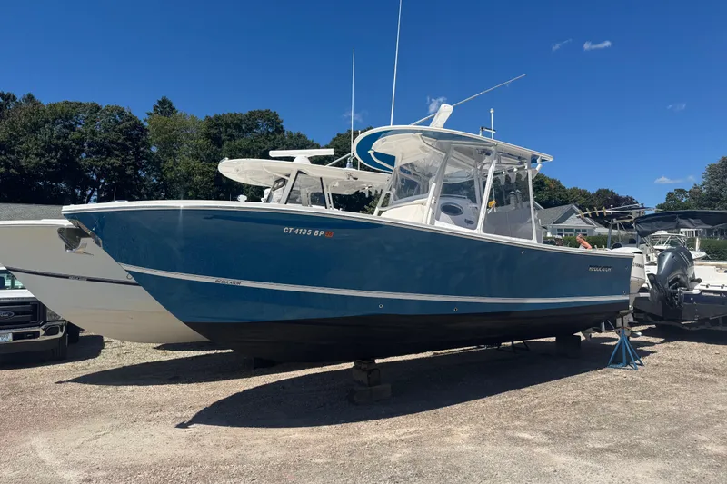 Slide: The Image of 2017 Regulator 28 boat in blue, parked on a gravel lot under a clear sky. - 2