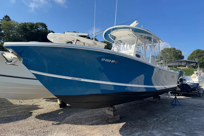 Slide: The Image of 2017 Regulator 28 boat with blue hull, parked on gravel, surrounded by trees and other boats. - 5