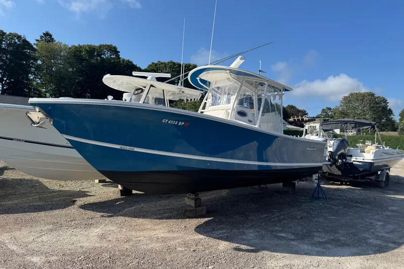 Slide: The Image of 2017 Regulator 28 boat in blue, parked on gravel with trees in the background. - 8