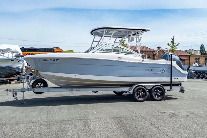 The Image of 2021 Robalo R247 Dual Console boat docked by a lush, green shoreline. - 0