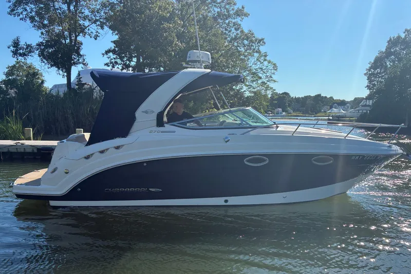 Slide: The Image of 2018 Chaparral 270 Signature boat on a sunny day, docked near lush greenery. - 2