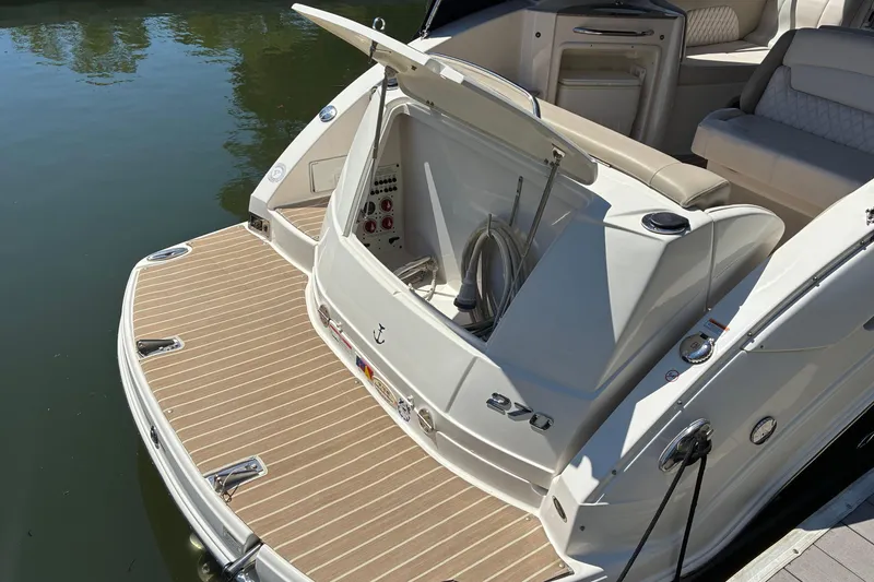 Slide: The Image of 2018 Chaparral 270 Signature boat with open storage compartment, docked on calm water. - 5