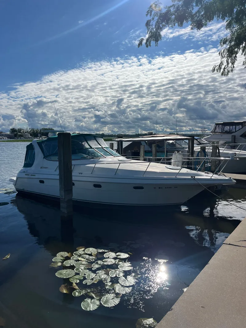 The Image of 1996 Cruisers Yachts 3375 docked by a serene lake under a partly cloudy sky. - 0