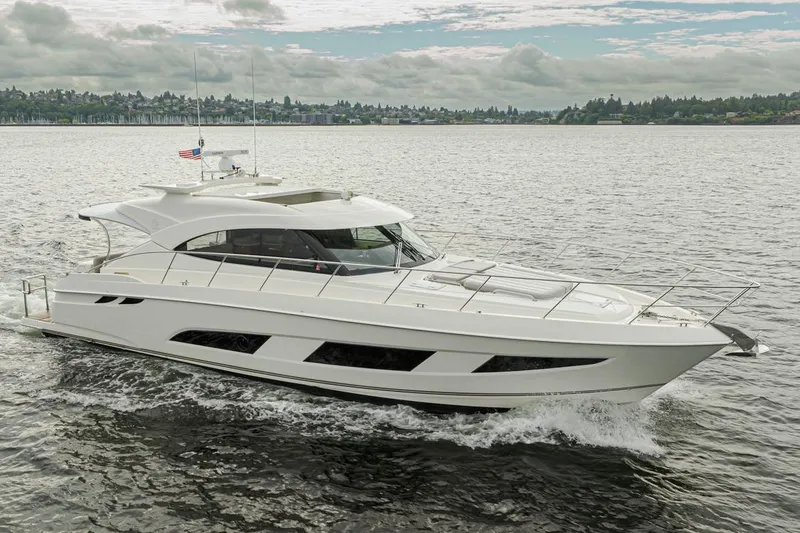 Slide: The Image of 2018 Riviera 4800 Sport Yacht cruising on a scenic lake under a cloudy sky. - 18