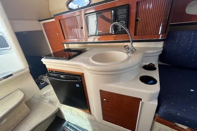 Slide: The Image of 2003 Sea Ray 260 Sundancer cabin with kitchenette, featuring sink, microwave, and mini fridge. - 31