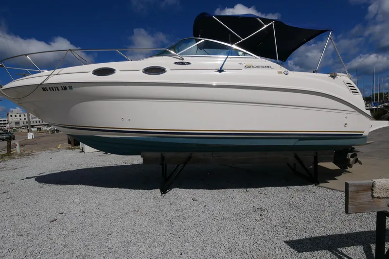 Slide: The Image of 2003 Sea Ray 260 Sundancer boat on dry dock, white hull, blue canopy, sunny day. - 7