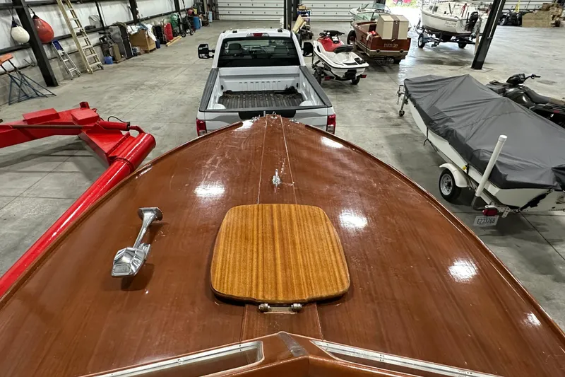 Slide: The Image of 1961 Lyman 21 Runabout boat in storage, wooden deck, surrounded by vehicles and equipment. - 15