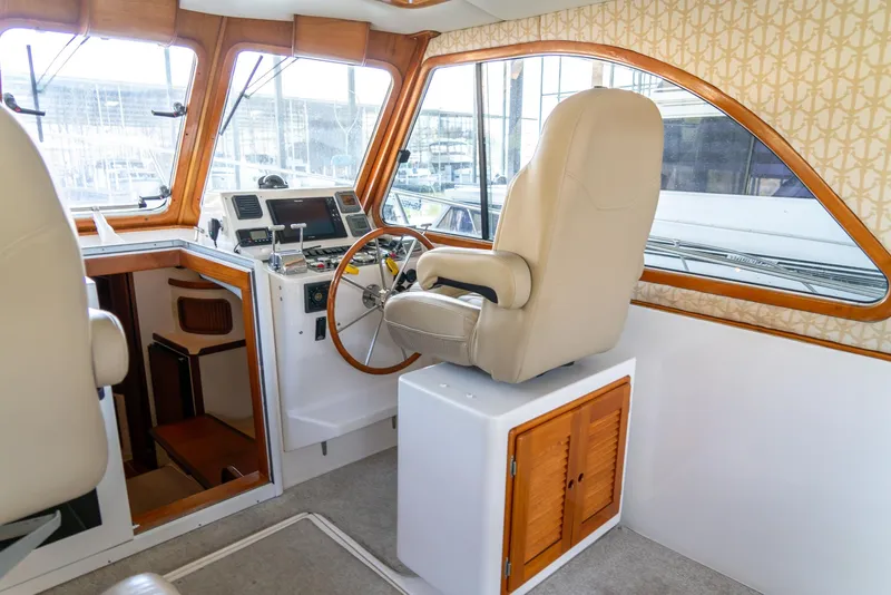 Slide: The Image of Captain's helm of a 2002 Legacy 34 Express boat with beige seating and wooden accents. - 27