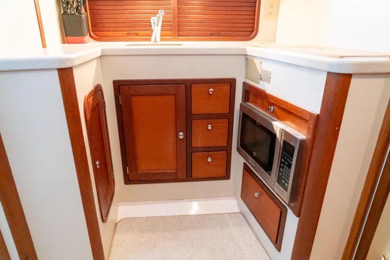 Slide: The Image of Compact kitchen area in a 2002 Legacy 34 Express boat with wooden cabinets and a microwave. - 37