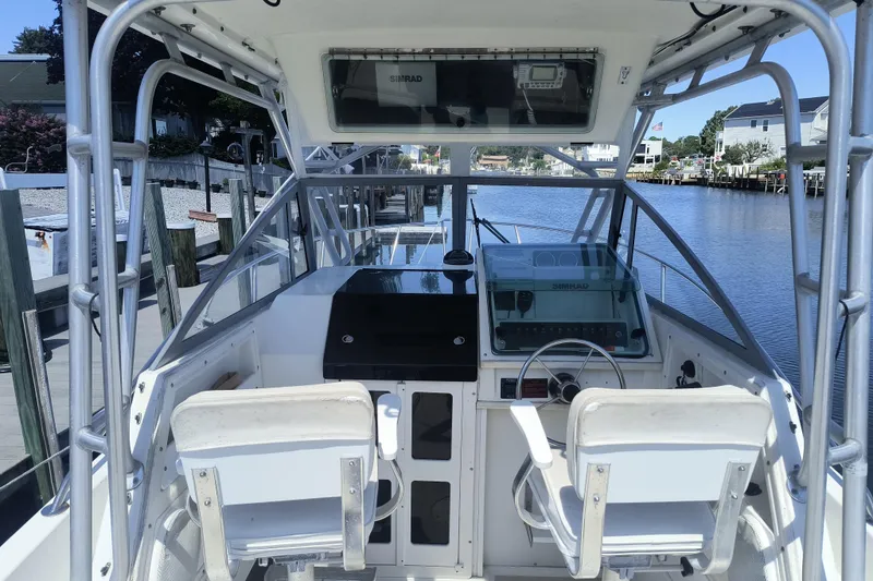 Slide: The Image of 1995 Robalo 2440 Walkaround boat interior with steering wheel and controls, docked by a canal. - 8